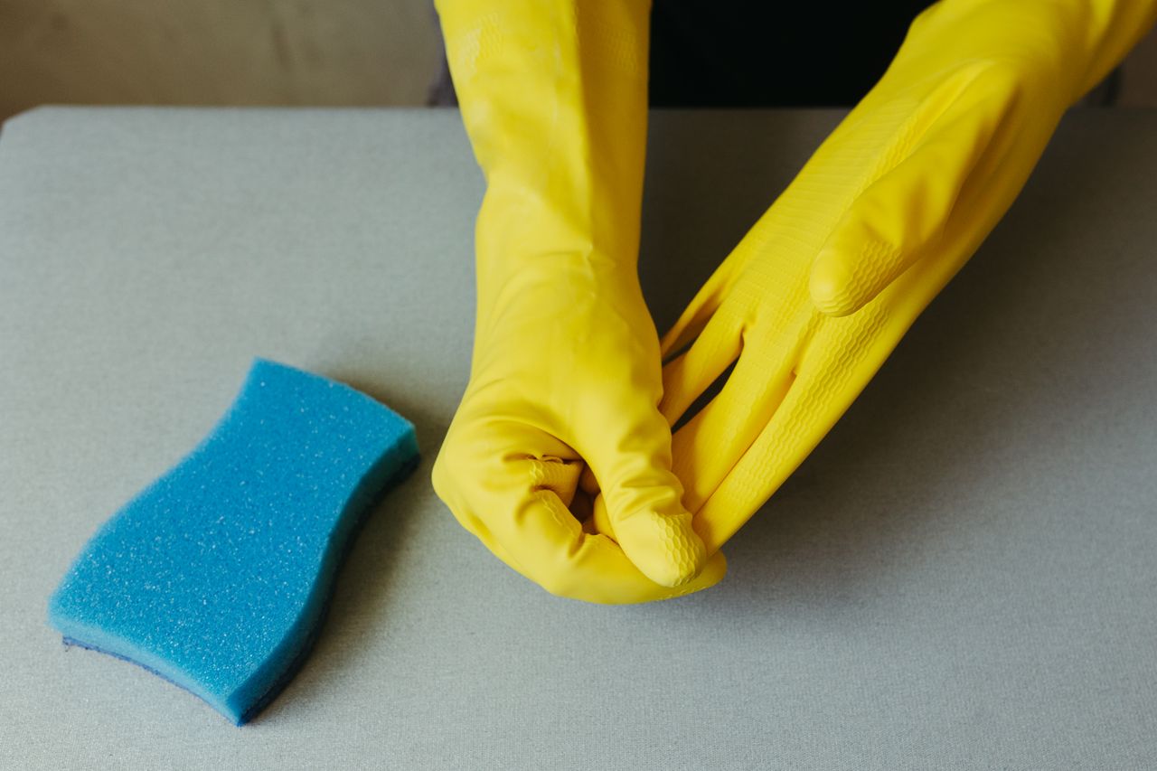 Gros plan sur des mains portant des gants jaunes à côté d'une éponge bleue sur une surface grise.